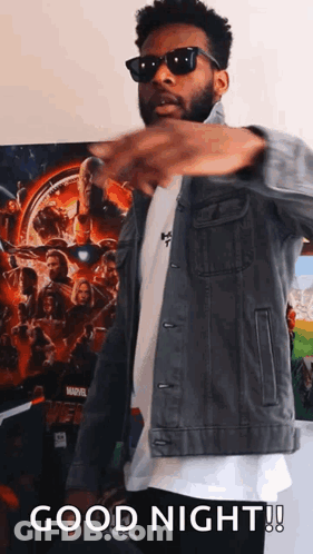 A Man Wearing Sunglasses And A Denim Jacket Is Standing In Front Of A Marvel Poster And Says Good Night . GIF