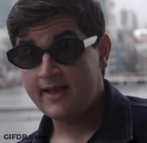 A Man Wearing Sunglasses And A Denim Jacket Looks At The Camera GIF