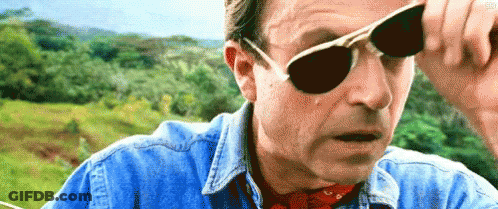 A Man Wearing Sunglasses And A Denim Shirt Is Looking At Something . GIF