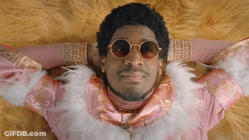 A Man Wearing Sunglasses And A Feather Boa Is Laying Down GIF