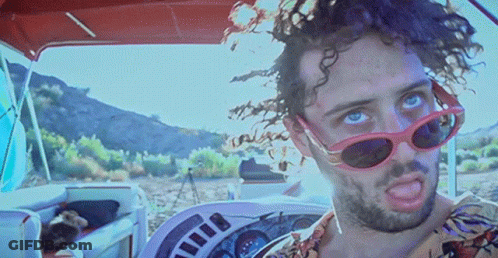 A Man Wearing Sunglasses And A Floral Shirt Is Driving A Boat GIF