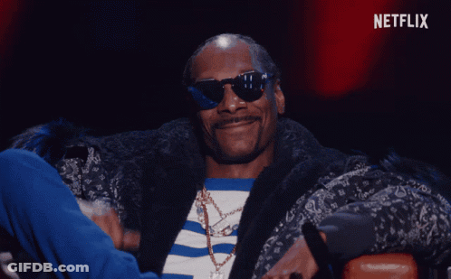 A Man Wearing Sunglasses And A Fur Coat Is Sitting In Front Of A Netflix Sign GIF