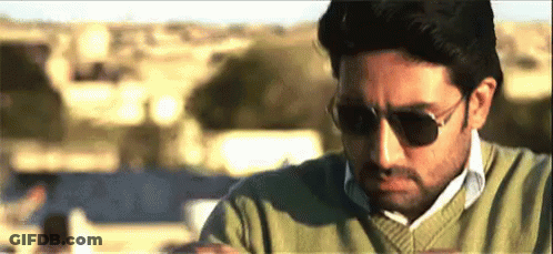 A Man Wearing Sunglasses And A Green Sweater Is Sitting On A Balcony . GIF