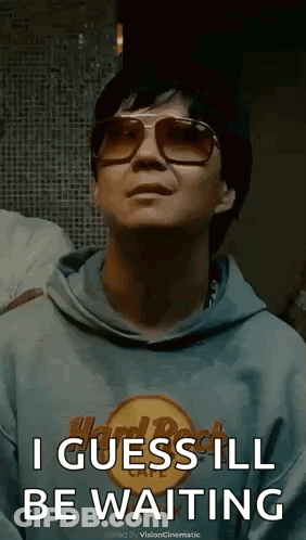 A Man Wearing Sunglasses And A Hard Rock Cafe Hoodie Is Waiting . GIF