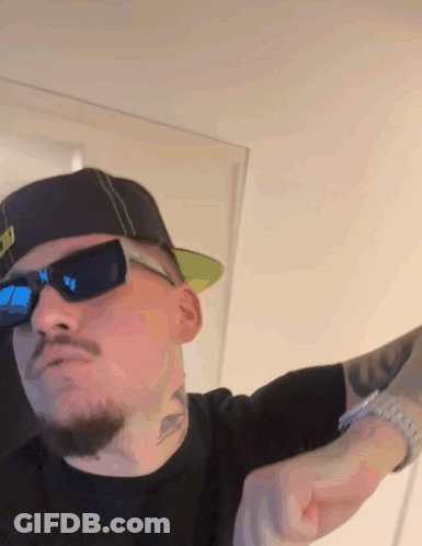 A Man Wearing Sunglasses And A Hat Has A Tattoo On His Arm That Says U. GIF