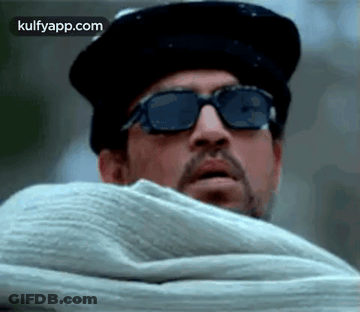 A Man Wearing Sunglasses And A Hat Is Covering His Face With A Blanket . GIF
