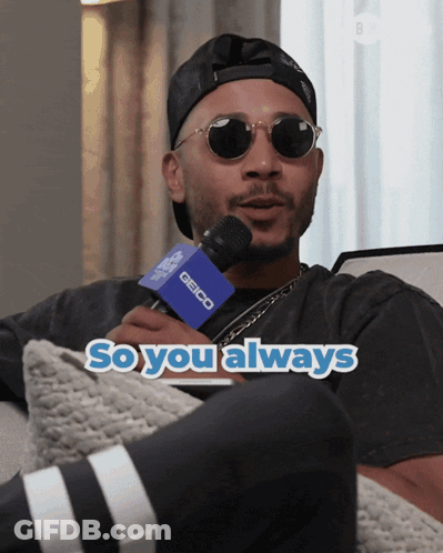 A Man Wearing Sunglasses And A Hat Is Holding A Microphone That Says Geico On It GIF