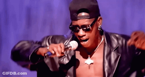 A Man Wearing Sunglasses And A Hat Is Singing Into A Microphone . GIF
