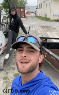 A Man Wearing Sunglasses And A Hat Is Smiling In Front Of A Boat GIF