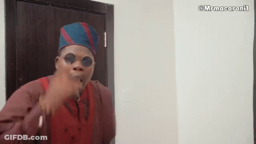 A Man Wearing Sunglasses And A Hat Is Standing In Front Of A Door And Making A Funny Face . GIF