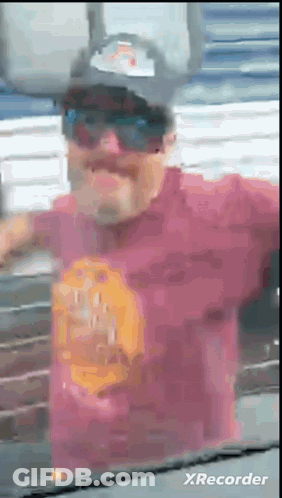 A Man Wearing Sunglasses And A Hat Is Standing In Front Of A Wall . GIF