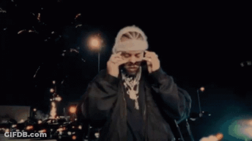 A Man Wearing Sunglasses And A Hat Is Standing In Front Of Fireworks . GIF
