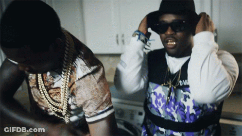 A Man Wearing Sunglasses And A Hat Is Standing Next To Another Man Wearing A Purple Vest GIF