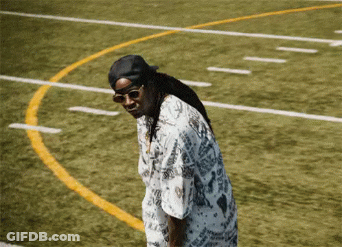 A Man Wearing Sunglasses And A Hat Is Standing On A Field GIF