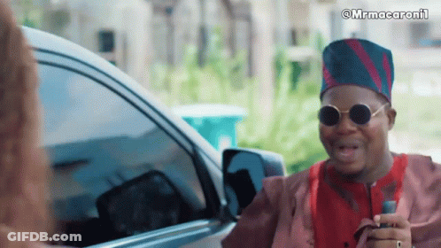 A Man Wearing Sunglasses And A Hat Is Talking To A Woman In Front Of A Car With The Caption Mrmacaronii GIF