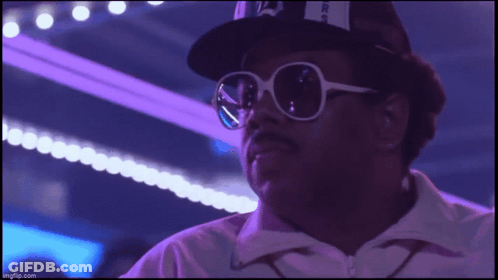 A Man Wearing Sunglasses And A Hat With The Letter A On It Looks At The Camera GIF