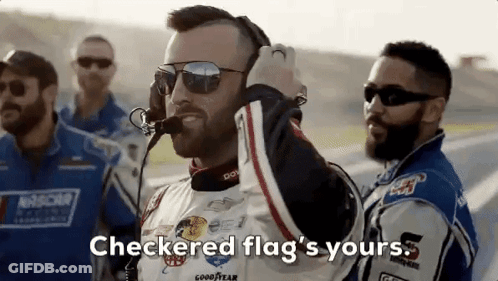 A Man Wearing Sunglasses And A Headset Is Standing Next To A Group Of Race Car Drivers On A Race Track . GIF