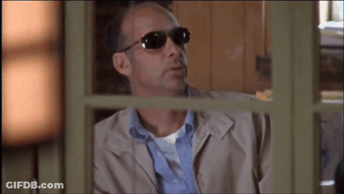 A Man Wearing Sunglasses And A Jacket Looks Out A Window GIF