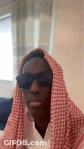 A Man Wearing Sunglasses And A Keffiyeh Is Making A Funny Face . GIF