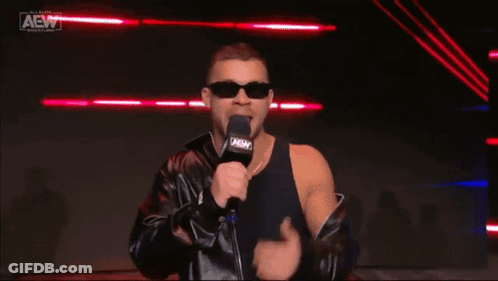A Man Wearing Sunglasses And A Leather Jacket Is Holding A Microphone And Covering His Eyes . GIF