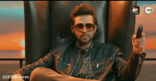 A Man Wearing Sunglasses And A Leather Jacket Is Sitting In A Chair Holding A Remote Control GIF
