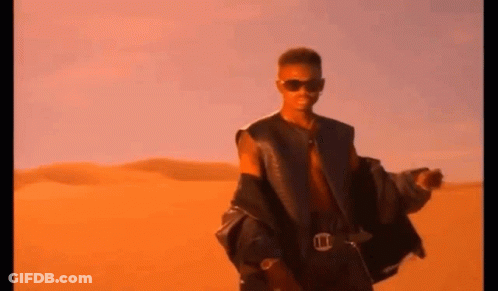 A Man Wearing Sunglasses And A Leather Jacket Is Standing In The Desert . GIF