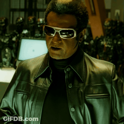 A Man Wearing Sunglasses And A Leather Jacket Stands In Front Of A Computer Monitor GIF