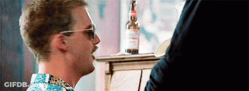 A Man Wearing Sunglasses And A Mustache Is Sitting At A Table With A Bottle Of Beer . GIF