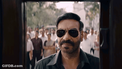 A Man Wearing Sunglasses And A Mustache Is Standing In Front Of A Crowd GIF