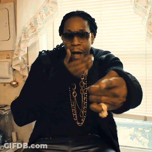 A Man Wearing Sunglasses And A Necklace Is Sitting In Front Of A Window In A Kitchen GIF