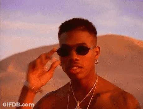 A Man Wearing Sunglasses And A Necklace Is Standing In The Desert . GIF