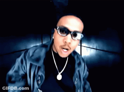 A Man Wearing Sunglasses And A Necklace Looks At The Camera With His Mouth Open GIF