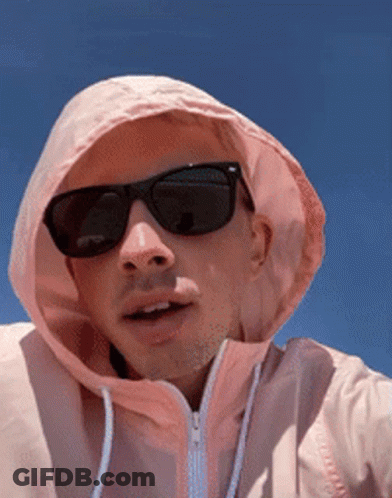 A Man Wearing Sunglasses And A Pink Hoodie Looks At The Camera GIF
