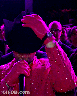 A Man Wearing Sunglasses And A Pink Jacket Is Holding A Microphone GIF