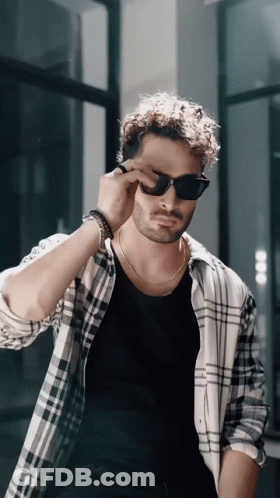 A Man Wearing Sunglasses And A Plaid Shirt Adjusts His Sunglasses GIF