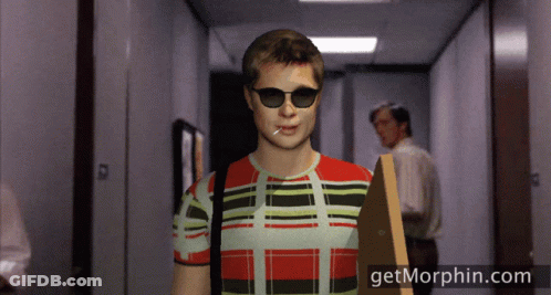 A Man Wearing Sunglasses And A Plaid Shirt Is Walking Down A Hallway With Getmorphin.com On The Bottom GIF