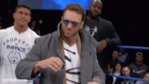A Man Wearing Sunglasses And A Property Of Impact Shirt Stands In A Boxing Ring GIF
