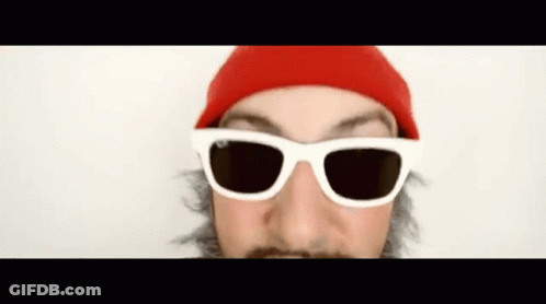 A Man Wearing Sunglasses And A Red Hat Looks At The Camera GIF