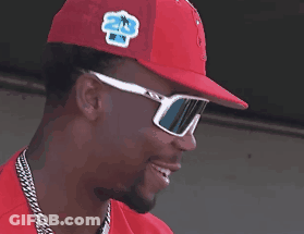 A Man Wearing Sunglasses And A Red Hat Smiles GIF