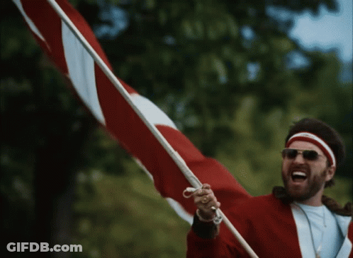 A Man Wearing Sunglasses And A Red Jacket Is Holding A Red And White Flag GIF