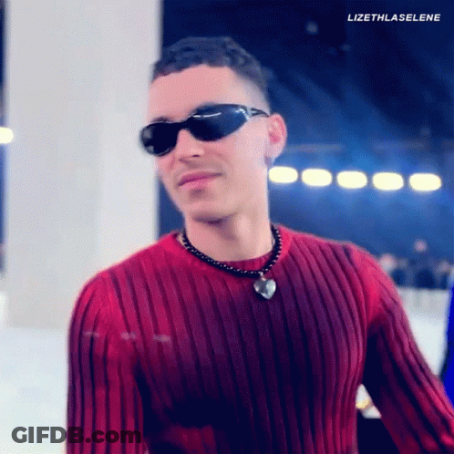 A Man Wearing Sunglasses And A Red Sweater Has A Heart Necklace Around His Neck . GIF