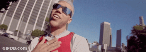 A Man Wearing Sunglasses And A Red Vest Is Standing In Front Of A City Skyline GIF