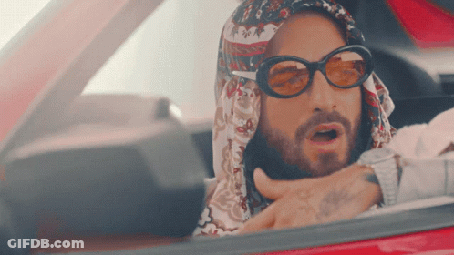 A Man Wearing Sunglasses And A Scarf Is Driving A Car GIF