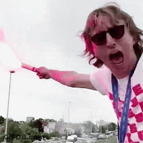 A Man Wearing Sunglasses And A Scarf Is Holding A Flare In His Hand . GIF