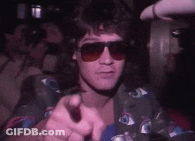 A Man Wearing Sunglasses And A Shirt With Eyes On It Is Pointing . GIF