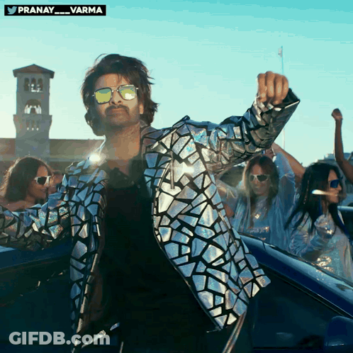 A Man Wearing Sunglasses And A Silver Jacket Is Dancing GIF