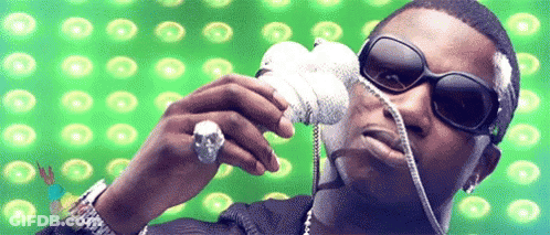 A Man Wearing Sunglasses And A Skull Ring Is Holding A Microphone In Front Of A Green Background GIF