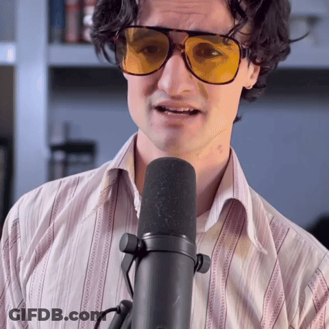 A Man Wearing Sunglasses And A Striped Shirt Is Speaking Into A Microphone GIF