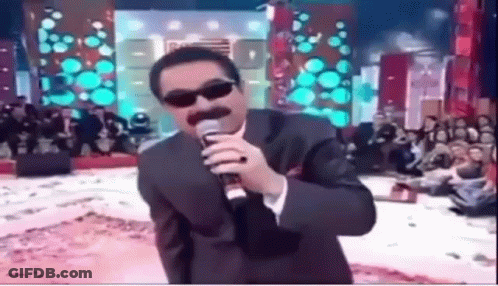 A Man Wearing Sunglasses And A Suit Is Singing Into A Microphone . GIF