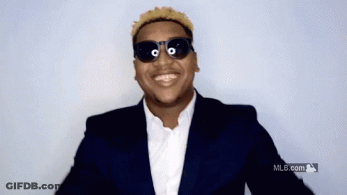 A Man Wearing Sunglasses And A Suit Is Smiling In Front Of A Mlb Logo GIF